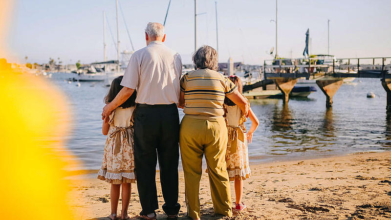 Old couple and two young girls standing at the beach with the back to the recipient.
