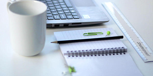 Ein Schreibtisch mit Laptop, Notizbuch und Tasse.