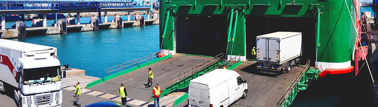 Bild der Beladung eines Frachtschiffs mit Autos und LKWs.