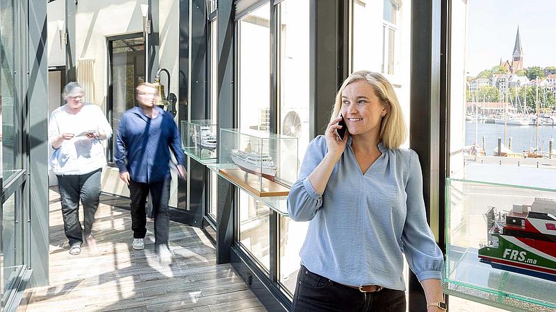 A women speaking on her telephone in a glass hallway with two people approaching in the background